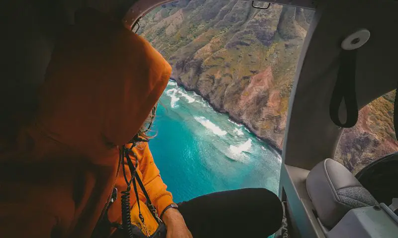 Hooded passenger leering out of doors open helicopter at the Kauai coast